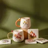 Escena de estilo con dos tazas retro "Bee Happy" y accesorios a juego, sobre fondo de tela verde oscuro - Happyideas