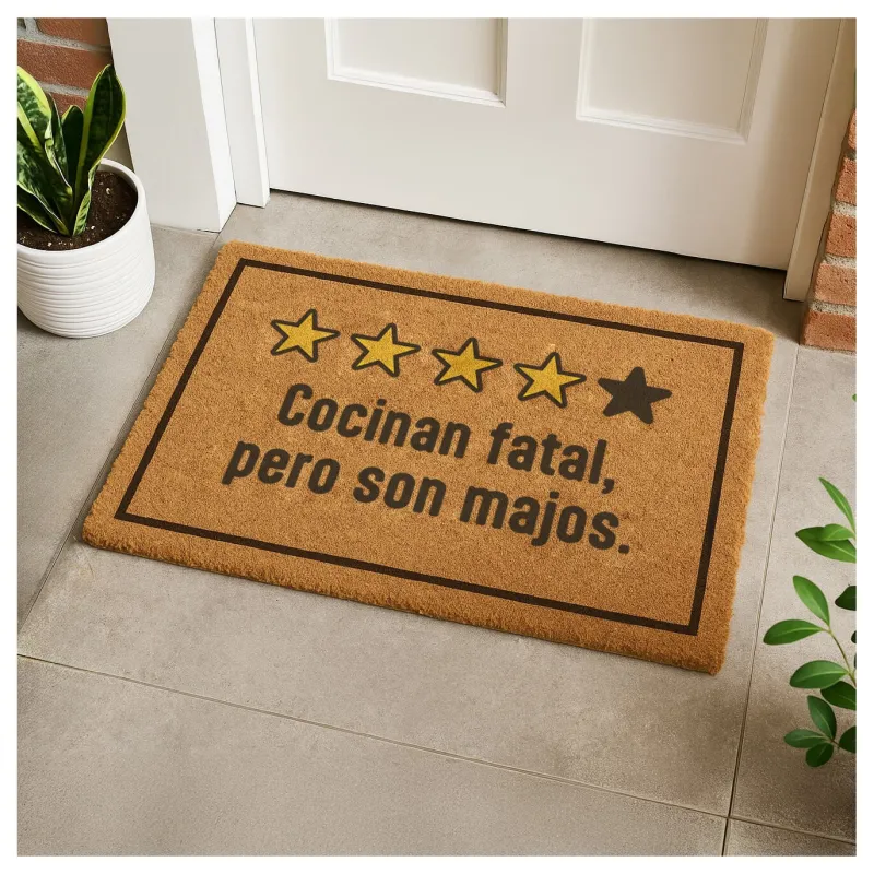 Felpudo "Cocinan fatal, pero son majos" colocado en la entrada de una puerta junto a plantas decorativas - Happyideas