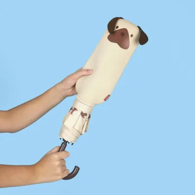 Mano sujetando un paraguas cerrado con funda con forma de cabeza de perro beige y orejas marrones, sobre fondo azul - Happyideas