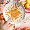 Plato Sol Cerámica, portada del producto, con motivo de sol radiante en tonos dorados sobre mesa con limones - Happyideas