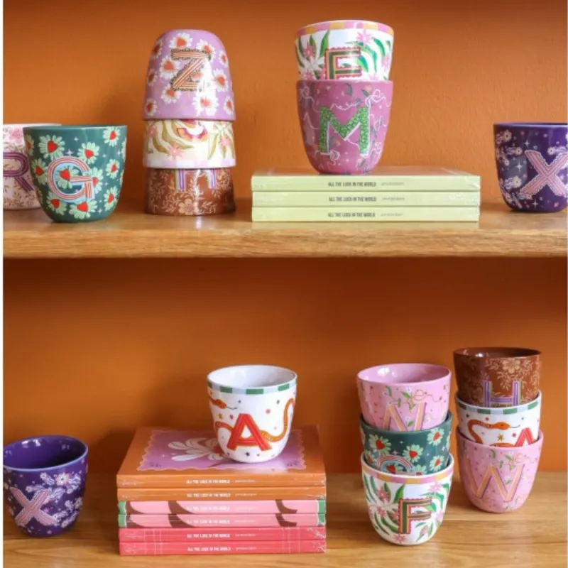 Taza Letra M junto a otras tazas monograma de distintos colores, sobre estantería con libros - Happyideas