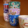 Taza Letra J junto a otras tazas monograma de distintos colores sobre superficie de madera - Happyideas