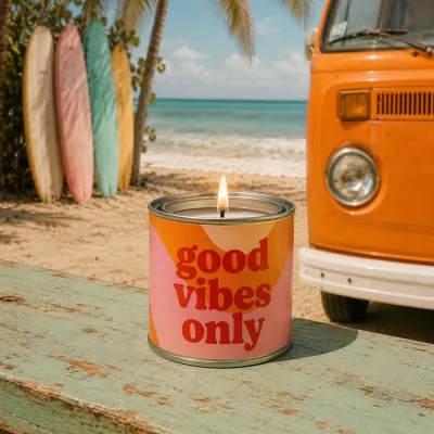 Vela en lata Good Vibes Only encendida en la playa junto a una furgoneta